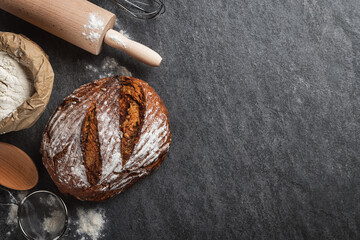 Poster - Whole loaf of fresh homemade bread with paper bag of flour on dark background with copy space top view.  Bakery background