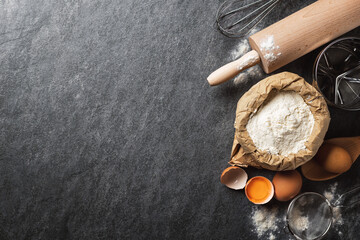 Poster - Ingredients for cooking baking dough, paper bag with flour, eggs, rolling pin and sieve on dark background with copy space top view.  Bakery background