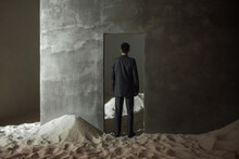 A Surreal Look, A Businessman In A Suit Stands Lost In The Doorway, Solution Of The Problems Has Not Been Found. Indoor Desert