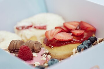 Canvas Print - Box of tasty donuts topped with cream, chocolates, and blackberries, vertical shot