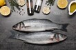 Fresh raw sea bass fish, seasonings and lemons on black table, flat lay