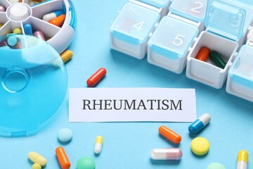 Card with word Rheumatism and pills on light blue background