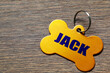 © New Africa - Yellow metal pet tag in shape of bone on wooden table, closeup. Space for text