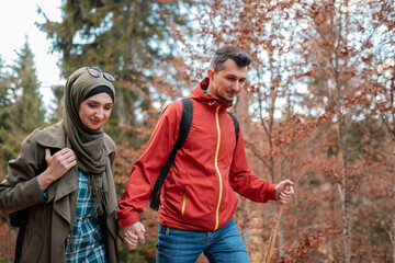 A young happy Muslim couple hiking in the autumn forest they are walking together with holding hands.