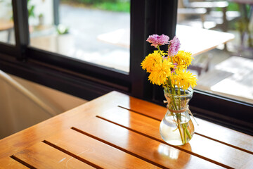 Wall Mural - A yellow flower in glass vase which is placed on the wooden table for decoration. Interior decor furniture and object photo, selective focus.