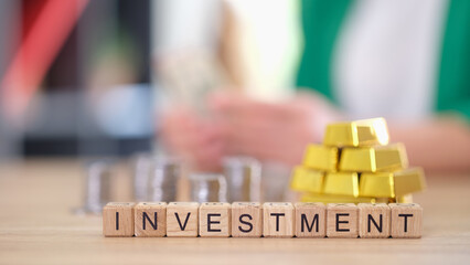 Wall Mural - Word investment with gold bars and stacks of coins on table.