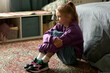 Little girl with sad expression sitting on floor along in her room