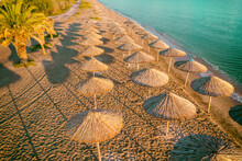 Tropical Beach Scenery With Sun Parasols And Palm Branches. Straw Sun Umbrellas On The Beach At Sunset. View Of Seascape From Above