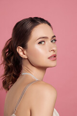 Young woman wearing elegant pearl necklace on pink background