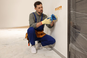 Poster - Electrician in uniform with insulating tape repairing power socket indoors