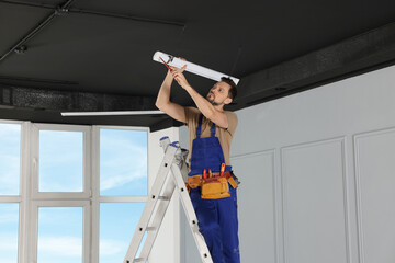 Poster - Electrician in uniform installing ceiling lamp indoors