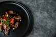 Korean Galbi Jjim, braised short ribs with spring onion and pepper in black plate on dark background