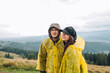 © bodnarphoto - Beautiful young couple man and woman in raincoats standing with smiles on their faces against the background of mountain views and posing for the camera with a serious face.