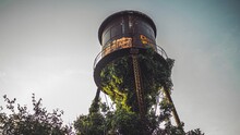 Low Angle Shot Of An Unused And Abandoned Water Tower With Trees Under Gray Sky