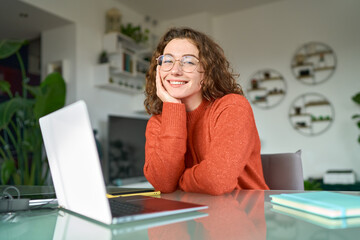 young smiling pretty business woman student sitting at table at home office with laptop computer loo