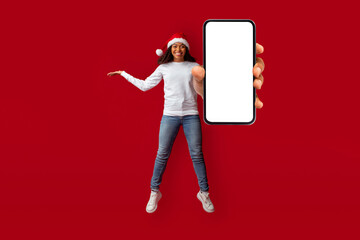 Happy pretty black woman in Santa hat showing smartphone, mockup