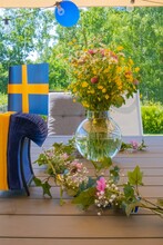 Vertical Shot Of A Vase With A Bouquet And Wildflowers On A Garden Table With A Swedish Flag