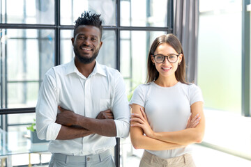 African woman and caucasian man looking at camera standing in office. Multicultural company managers team portrait