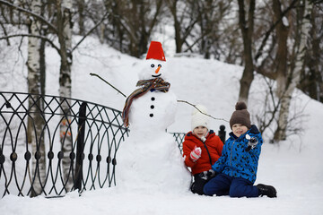 Wall Mural - Children in the park in winter. Kids play with snow on the playground. They sculpt snowmen and slide down the hills.