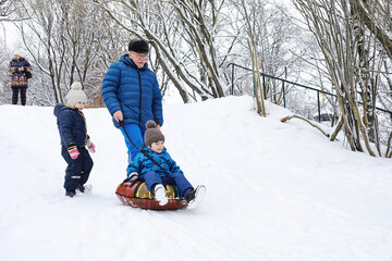 Wall Mural - Children in the park in winter. Kids play with snow on the playground. They sculpt snowmen and slide down the hills.