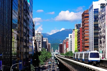 Wall Mural - A metro train traveling on the elevated rail of Taipei MRT between office towers under blue sky ~ View of a public transportation system in Taipei, the capital city of Taiwan, on a beautiful sunny day