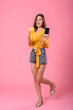 Beautiful Asian woman in summer holding smartphone and credit card online shopping on pink background.
