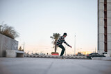 caucasian guy in striped pullover sneakers having fun on a skateboard in the city at sunset on a clear day