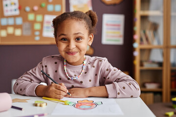 cute successful learner of primary school looking at camera with smile while sitting by table and dr