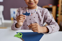 Close-up Of Cute Little Learner Of Nursery School Holding Tiny Paper Ship Of Navy Blue Color While Sitting By Desk In Front Of Camera
