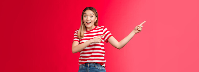 Hey hurry up look. Enthusiastic excited cute asian blond urban girl pointing left showing incredible offers, raise eyebrows thrilled talk camera smiling delighted stand red background impressed