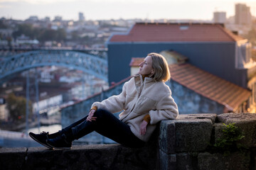 A female tourist rest on a masonry wall in Porto, Portugal.