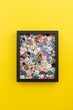 Pile of colorful sewing buttons in a black frame isolated on yellow background