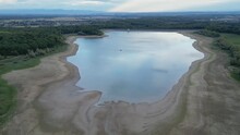 Flight Over The Michelbach Lake Dam (Upper-Rhine, Alsace, France) By Drought And Cloudy Weather In Summer With A Very Low Water Level, In The Evening At Sunset With Village And Mountains In Background