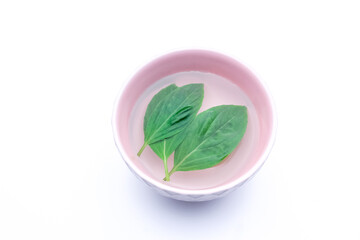 Three Green fresh basil leaf in the clean water with a small pink color cup isolated on white background.