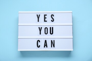 Lightbox with phrase Yes You Can on light blue background, top view. Motivational quote
