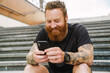 Young handsome bearded tattooed redhead smiling man with phone