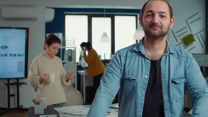 Wall Mural - Portrait of confident man entering frame posing with arms crossed and smiling in busy startup office. Relaxed employee acting casual looking at camera in marketing department of small company.