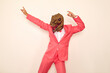 Weird crazy guy in wacky dinosaur mask enjoying free time and having fun at party. Happy confident young man wearing funky pink suit and silly ugly dino mask dancing against background of white wall