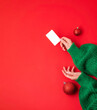 Christmas shopping concept. Flat lie hands in a green sweater with bonus card. Banner on a red background