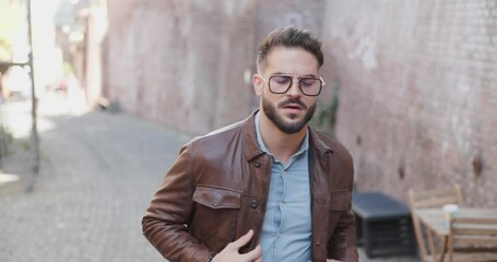 Wall Mural - project video of sexy stylish bearded man outside in an old city walking and looking around, adjusting jacket and glasses 