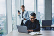 © Дмитрий Ткачук - A businessman is working on a laptop while talking while his colleague is listening. Work in a modern bright office