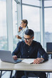 © Дмитрий Ткачук - A businessman is working on a laptop while talking while his colleague is listening. Work in a modern bright office