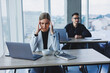 © Дмитрий Ткачук - A female manager sits at a desk using a laptop in a modern office with a colleague in the background. Working atmosphere in an office with large windows.
