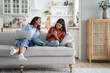 © DimaBerlin - Independent everyday teen girl keeps secrets from mom by hiding phone screen and avoiding surveillance. Smiling young woman with laptop on lap sits on sofa trying to make friends with daughter