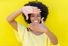 Happy Young Woman Making Frame With Hands In Front Of Yellow Wall
