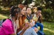 © Westend61 - Smiling young woman with friends eating snack sitting in park