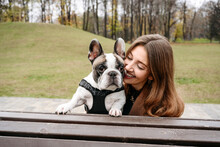 Cheerful Woman Embracing French Bulldog On Bench At Park