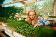 © StratfordProductions - Young caucasian woman in checked shirt examining plants in trays at plant nursery