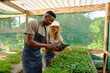 © StratfordProductions - Young multiracial couple wearing aprons using digital tablet while gardening in plant nursery