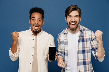 Wall Mural - Young two friends happy men wear white casual shirts together use point finger on mobile cell phone with blank screen workspace area do winner gesture isolated plain dark royal navy blue background.